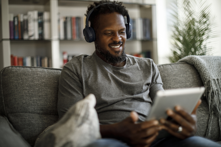 Young smiling man with wireless headphones using digital tablet at home