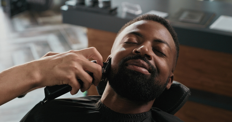 Shot of a handsome young man trimming his beard at the barber