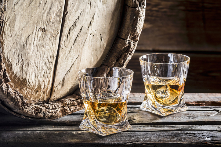 Two glasses of whiskey on the rocks in front of an old wooden barrel