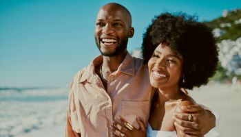Young happy black couple smiling, bonding and walking on beach together during summer on the weekend. Loving husband and wife embracing, enjoying a romantic getaway and relaxing on honeymoon