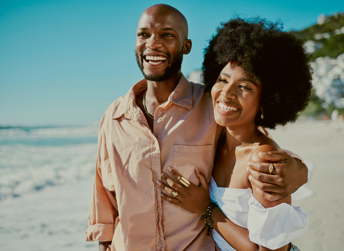 Young happy black couple smiling, bonding and walking on beach together during summer on the weekend. Loving husband and wife embracing, enjoying a romantic getaway and relaxing on honeymoon