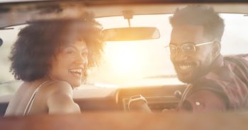 Driving young, trendy and smiling couple in car on a romantic drive, holiday or getaway in summer. Happy, fun and positive African best friends on a roadtrip or vacation listening to music.