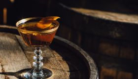 Manhattan Bourbon Whiskey Cocktail In Vintage Crystal Hotel Glass Orange Garnish Atop Wood Barrel