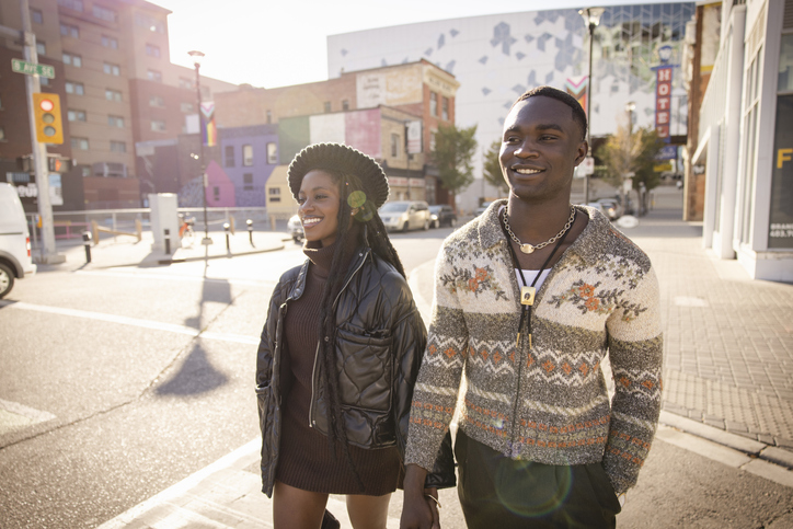 Happy young couple holding hands, walking in sunny city