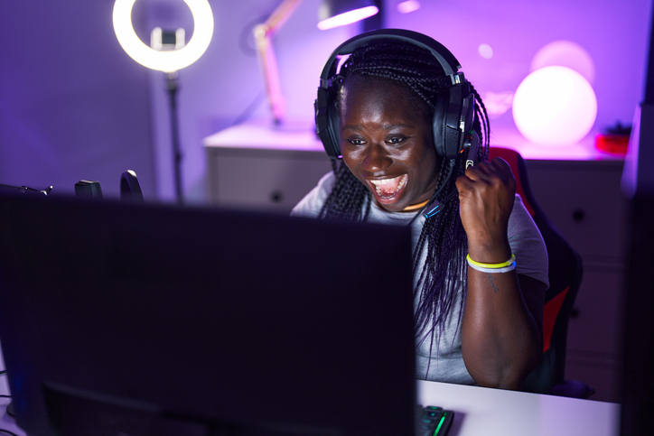 African american woman streamer playing video game with winner expression at gaming room