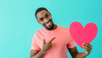Portrait of an smiling young man pointing to pink heart in big smile, valentine"u2019s day love, find love in dating concept