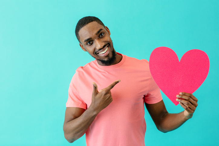 Portrait of an smiling young man pointing to pink heart in big smile, valentine"u2019s day love, find love in dating concept