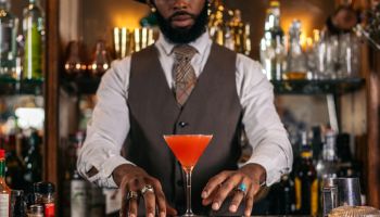 Cutout of a black bartender offering a cocktail served in a martini glass in a traditional cocktail bar