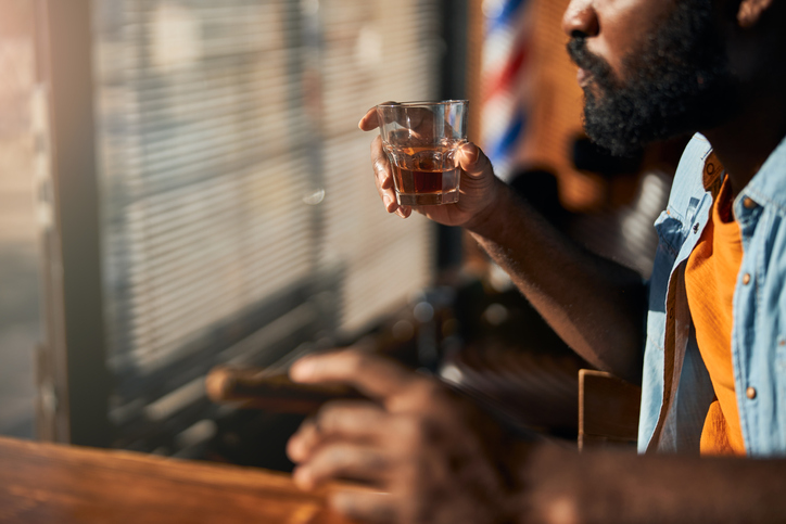 Bearded young man smoking cigar and drinking whisky