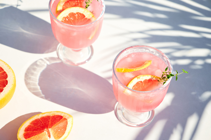 Chilled cocktails with fresh grapefruit juice, served with a sprig of thyme and fresh fruit slices. Refreshing summer cocktails with citrus fruits.
