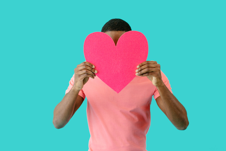 Portrait of a young man holding pink heart in front of head with face obscured, valentineâs day love, give your heart concept