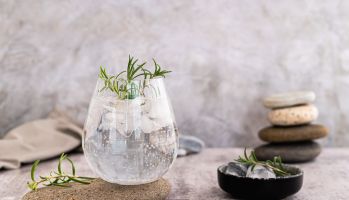 Gin tonic with ice and rosemary in a glass on a stone on the table