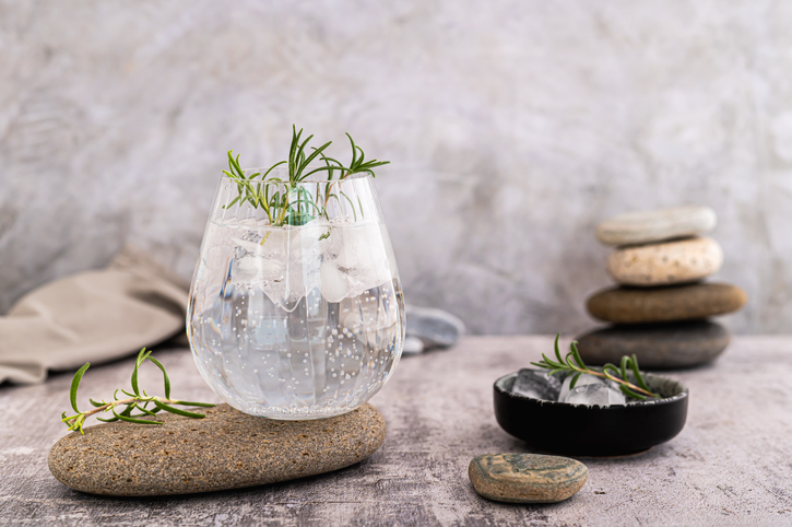 Gin tonic with ice and rosemary in a glass on a stone on the table