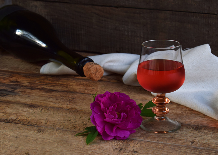 A glass of red wine, bottle and rose on rustic wood table. Valentines Day, Birthday, Mother's day, March 8, Wedding still life. Concept greeting card. Copy space for text