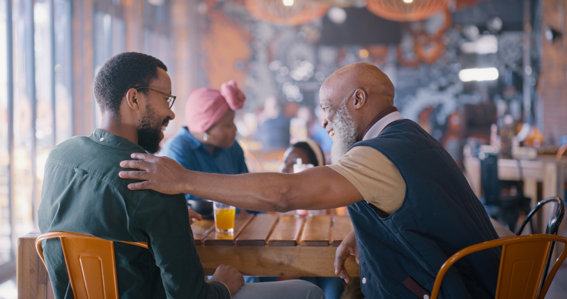 Senior father, man and restaurant with family, dinner and embrace with conversation, memory and bonding. Elderly dad, son and African people with love, chat and happy together in diner for reunion