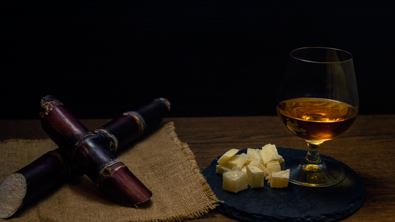 Glass of cane rum with pieces of cane on rustic wooden table and dark background