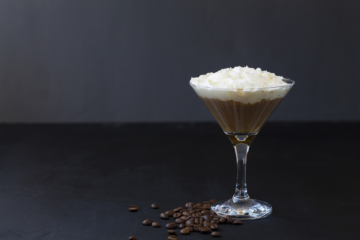 coffee cocktail in martini glass with whipped cream on dark background. Alcoholic or non-alcoholic cocktail with liqueur, whiskey, white cream. copy space.