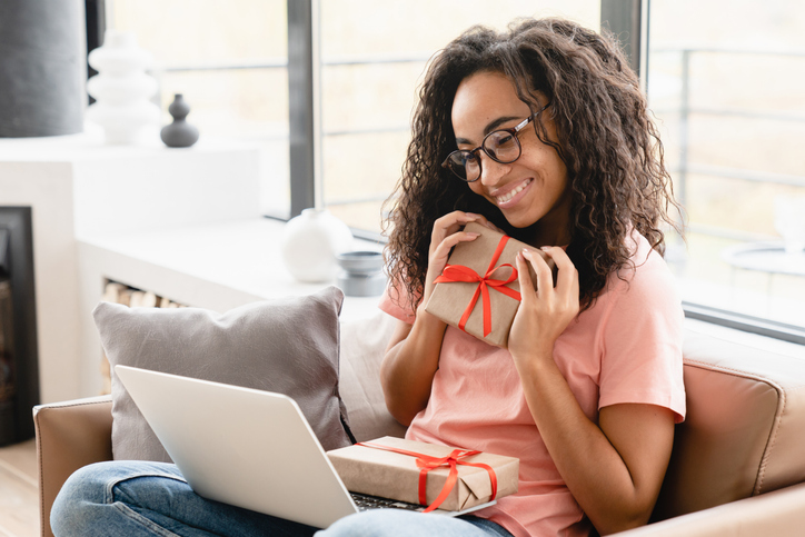Vlogging blogging. Young happy cheerful african woman housewife showing presents for Christmas New Year birthday anniversary Valentine`s Day on laptop having videocall online at home