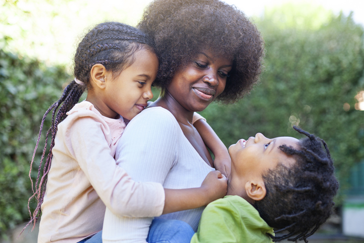 Happy African Mother Carrying Son And Daughter As They Play In Backyard