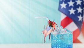 4th of July Holiday background. Cocktail with blue liqueur, American flag and festive straw against background of old turquoise board and sun rays. Patriotic American Flag drinks. Mock up.