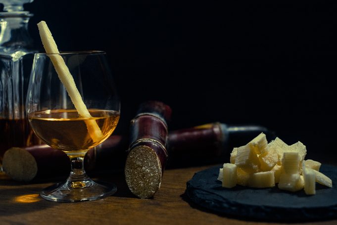 Glass of cane rum with pieces of cane on rustic wooden table and dark background