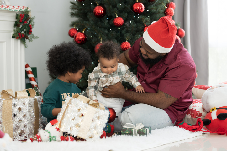 Christmas holiday. Happy family and gift box on Christmas day. African American family opening gift boxes together on Christmas day at home. Father gives gift box to his son