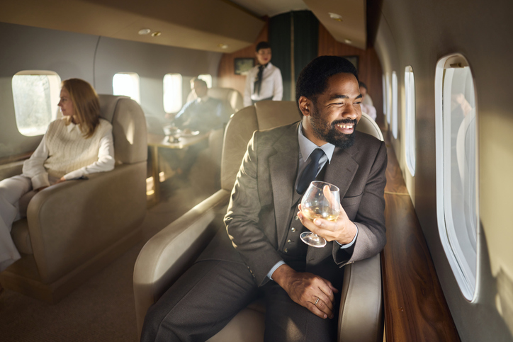 Happy black businessman day dreaming during flight in full corporate jet.