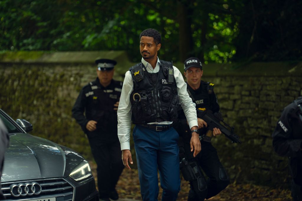 Three police officers, one in a vest, standing near a parked Audi car in a wooded area at night.