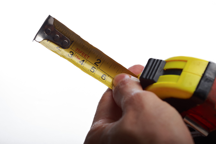 Human hand extending a yellow measuring tape rule isolated on a white studio background.