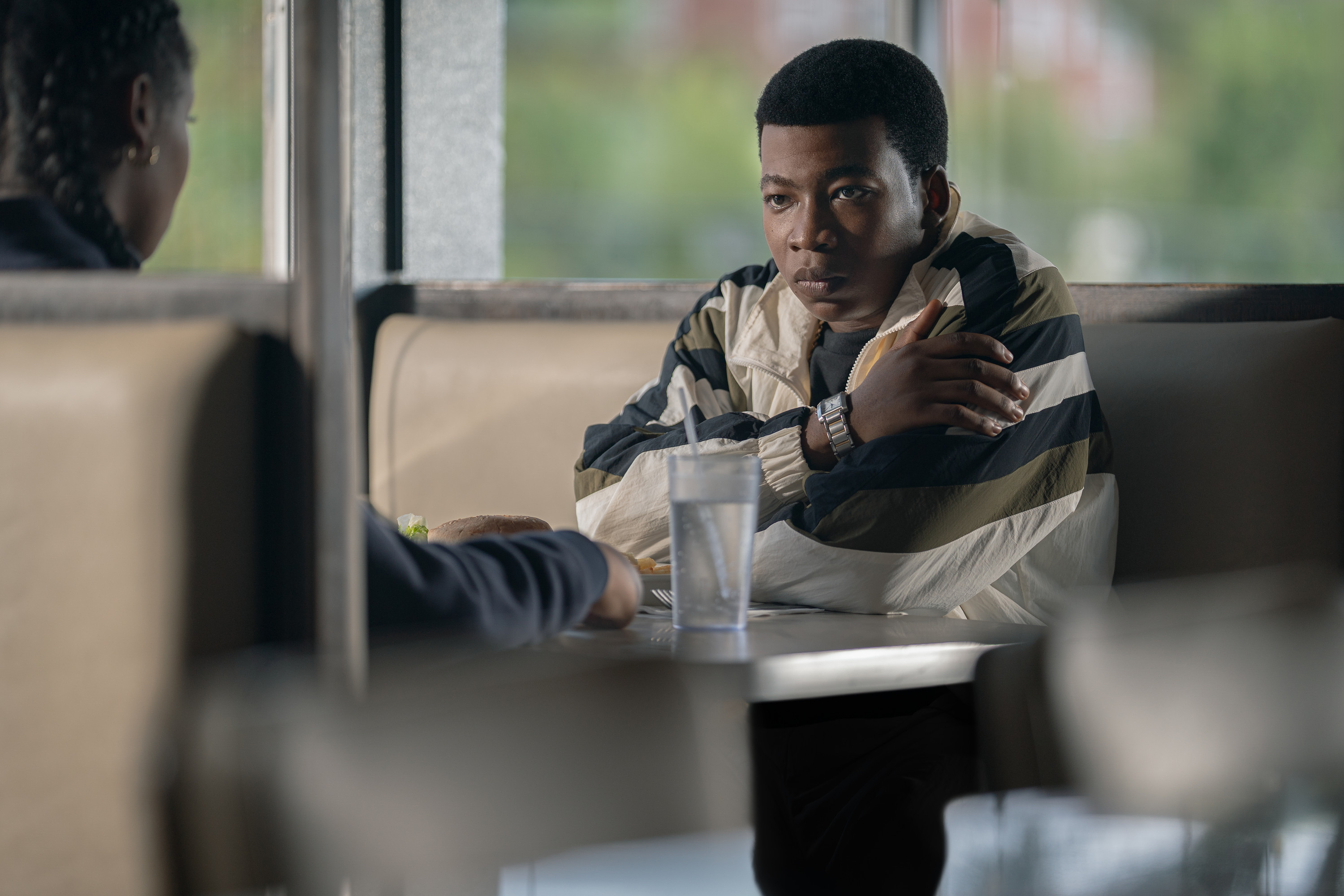 A man in a striped jacket sitting at a table, looking pensive and lost in thought.