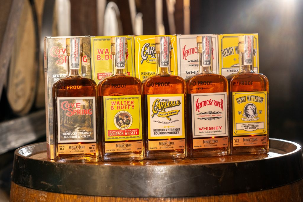 Assortment of Kentucky bourbon whiskey bottles, including brands like Evan Williams, Walter B. Duffy, and Henry Watterson, displayed on a wooden barrel.