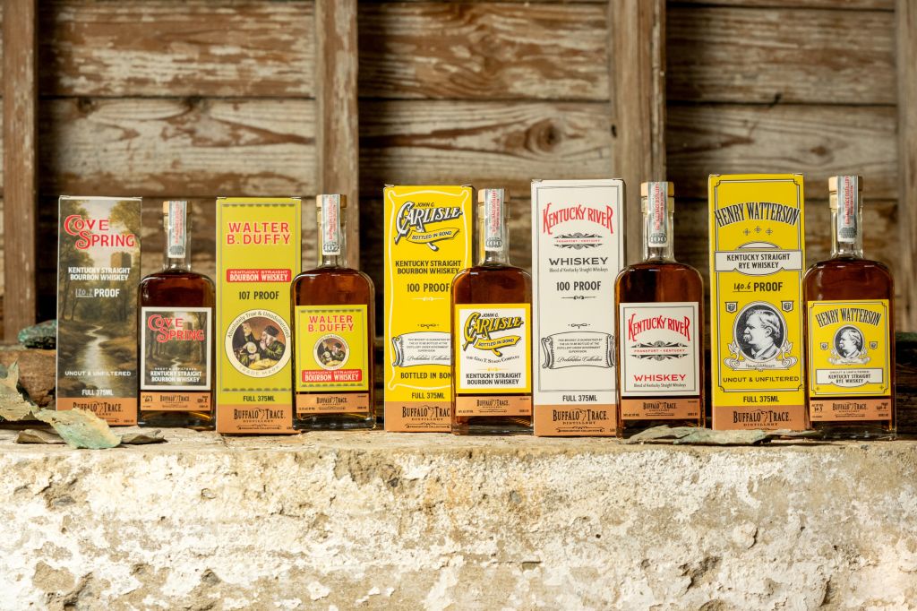 Assortment of vintage Kentucky bourbon whiskey bottles, including Carlisle, Kentucky River, and Henry Watterson brands, displayed on a wooden surface.