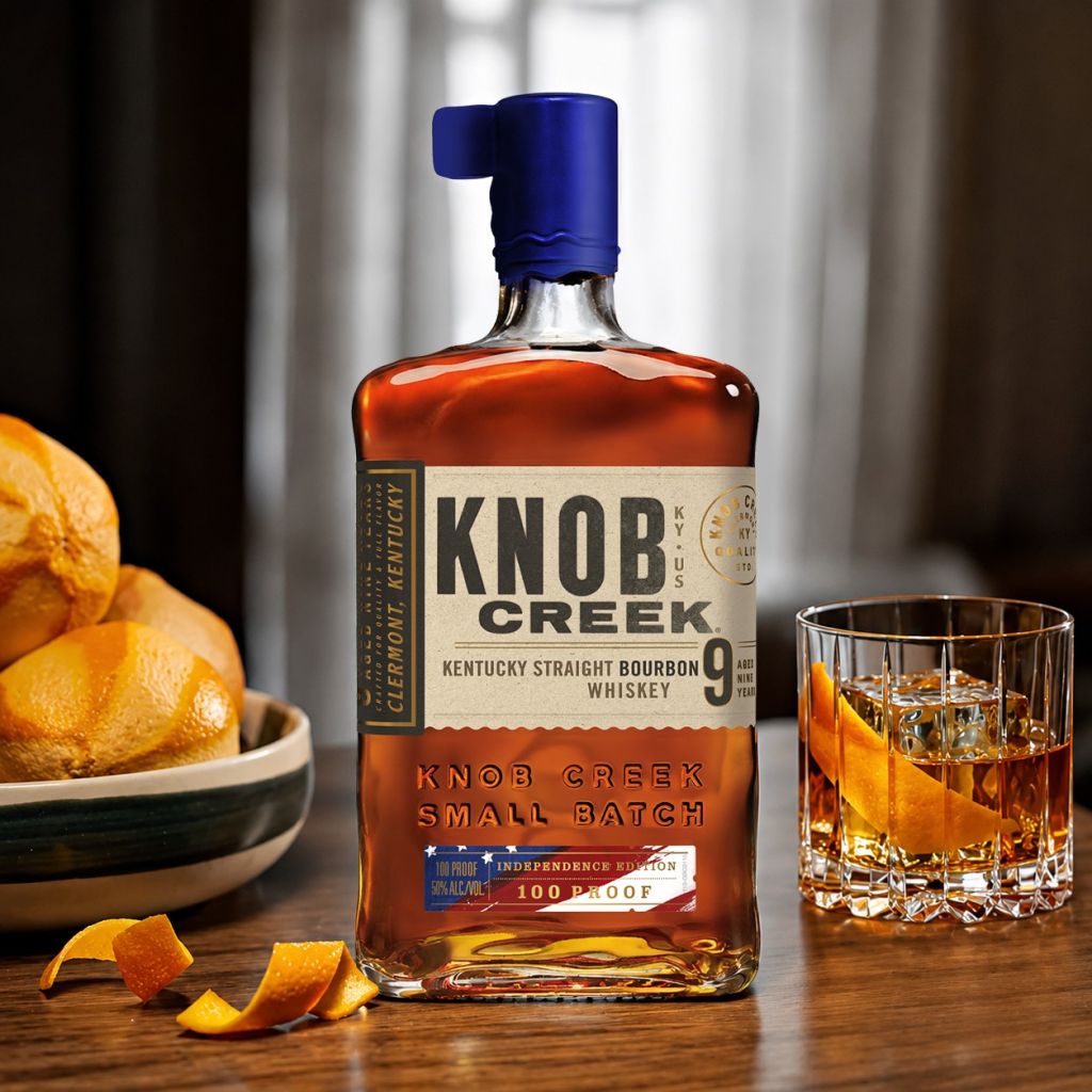 A bottle of Knob Creek Kentucky straight bourbon whiskey, with a glass of the amber-colored liquor on a table with orange slices.