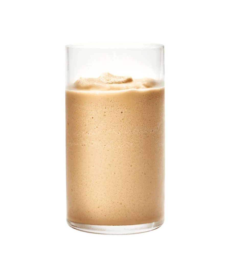 A glass filled with a creamy, frothy, light brown beverage, likely a milkshake or smoothie.