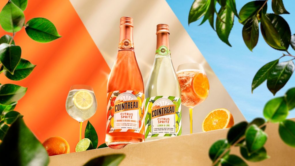 Two bottles of Cointreau Citrus Spritz liqueur with orange slices and greenery against a colorful background.