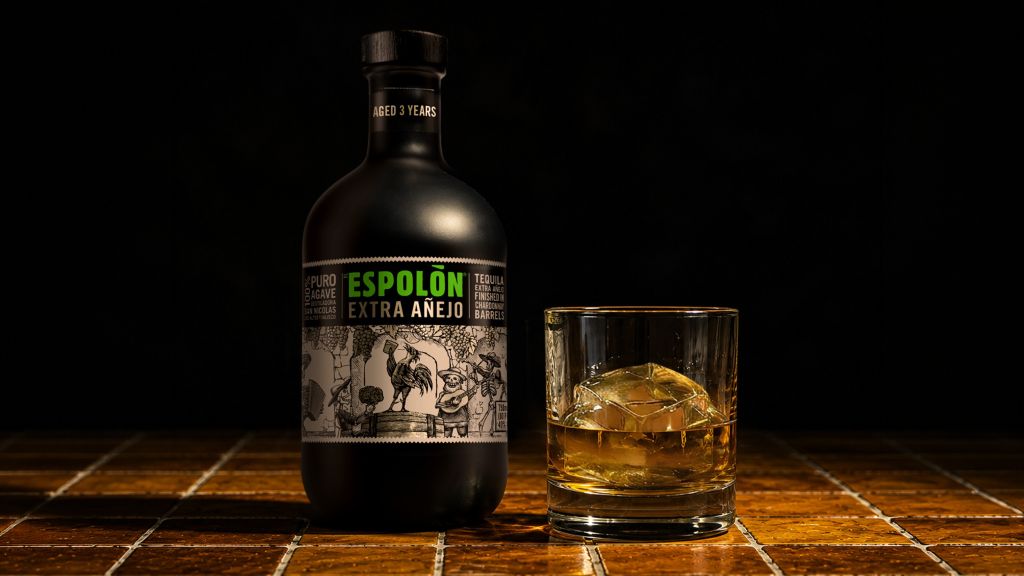 A bottle of Espolon Extra Anejo tequila and a glass of amber-colored liquor on a wooden surface.