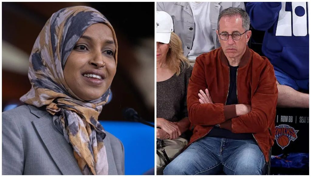 A smiling woman wearing a headscarf stands at a podium, while a man in a red jacket stands with his arms crossed in the background.