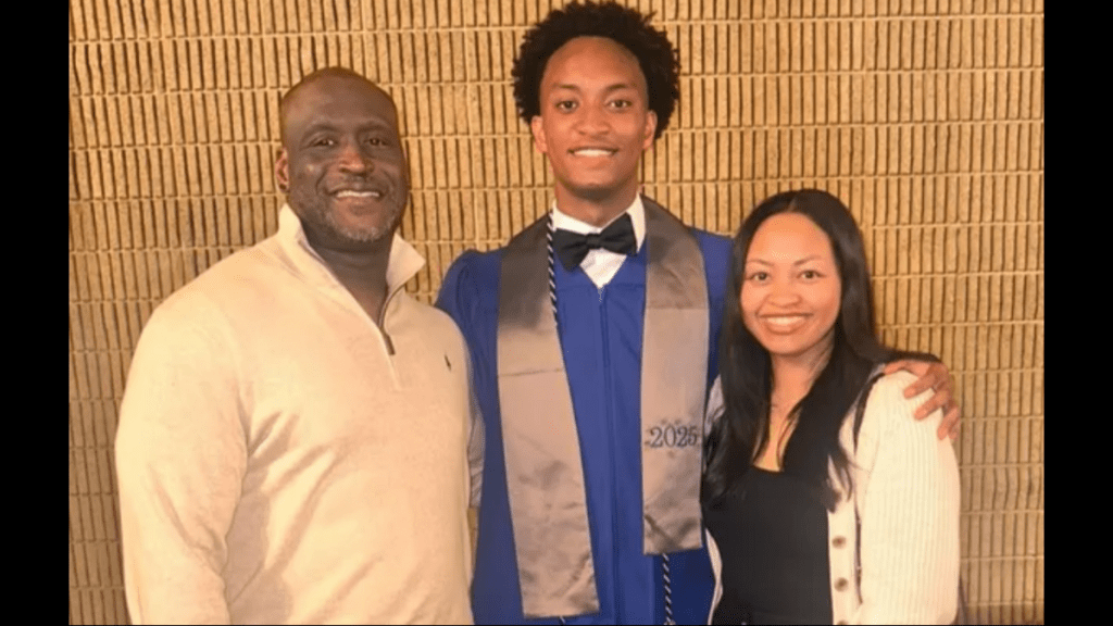 Three people posing for a photo - a smiling man in a beige sweater, a young man in a blue graduation gown, and a smiling woman in a black sweater.