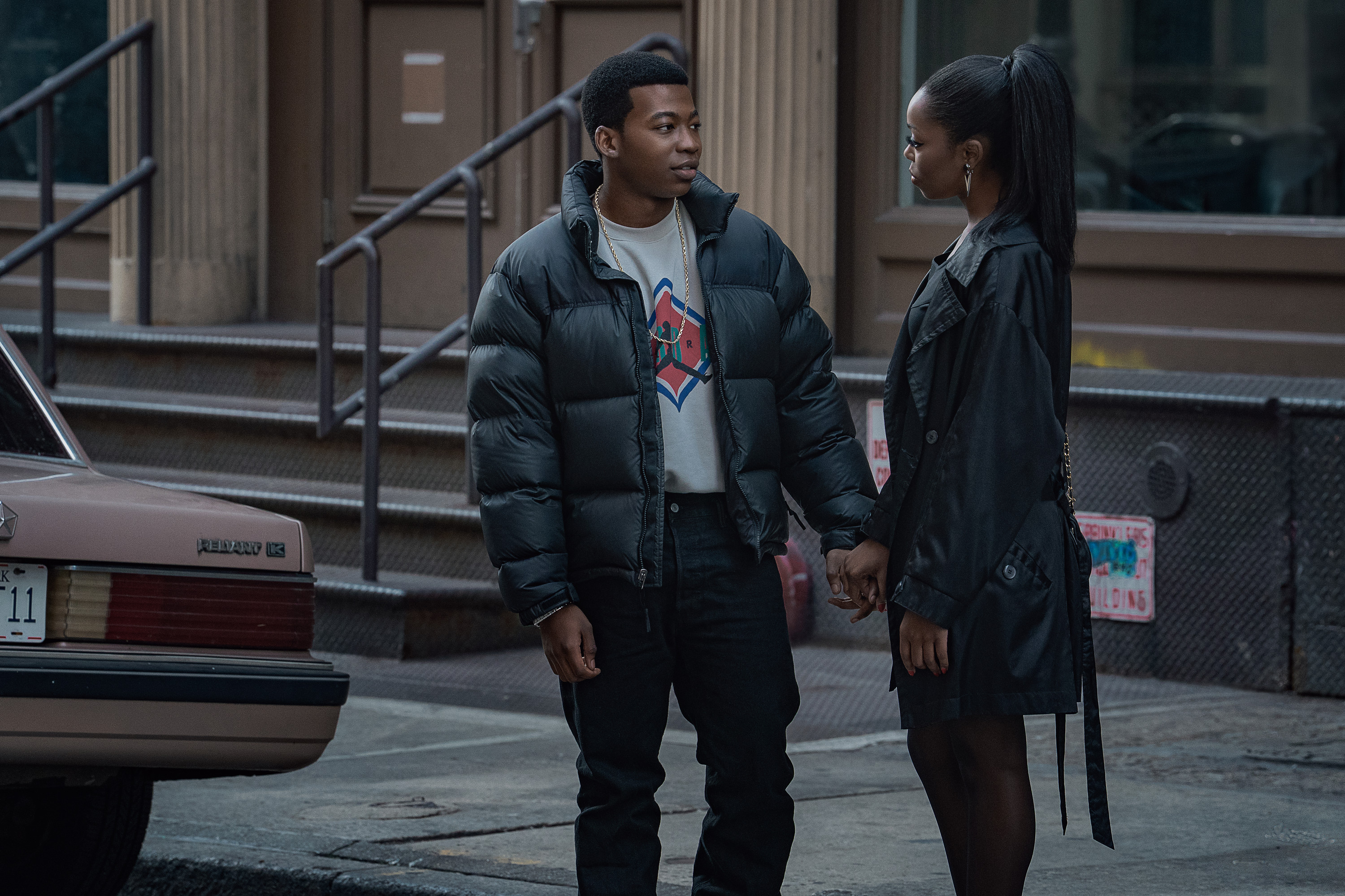 Two young people, a man and a woman, standing on a city street and looking at each other.
