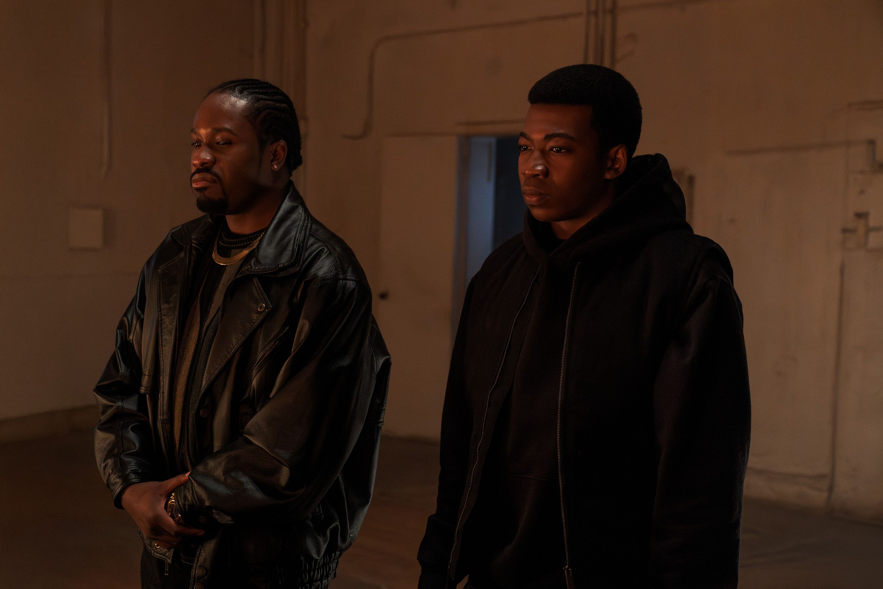 Two men in black jackets standing in a dimly lit hallway.