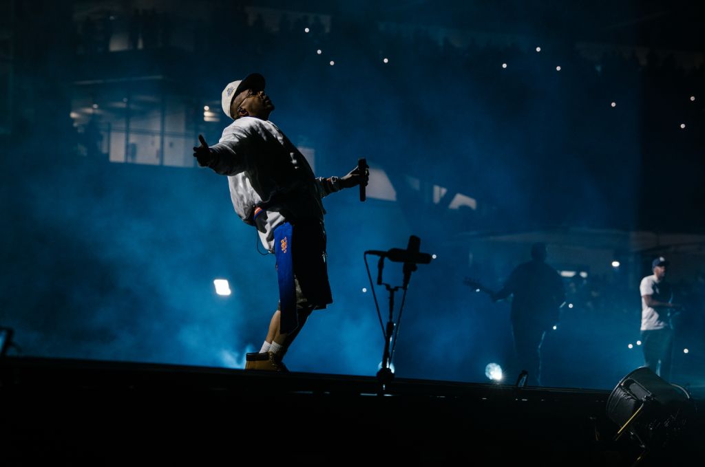 A person in a dark outfit performing on a dimly lit stage, with spotlights and smoke creating a dramatic atmosphere.