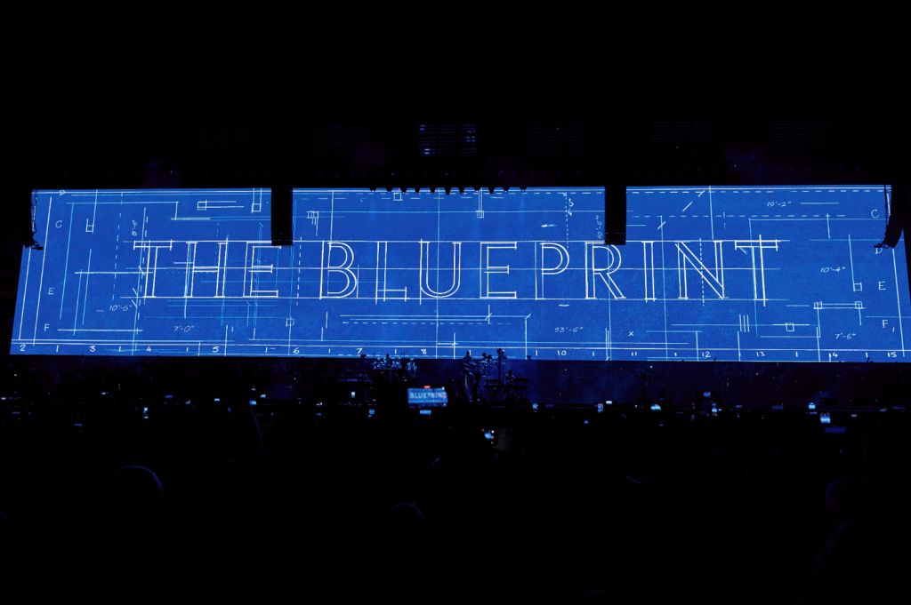 The Blue Print text displayed on a large projection screen in a dark venue, surrounded by an audience.