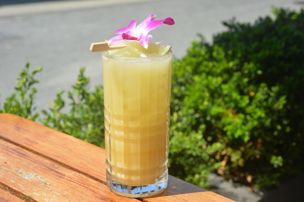 A tropical cocktail with a pink orchid garnish, served on a wooden table with lush greenery in the background.