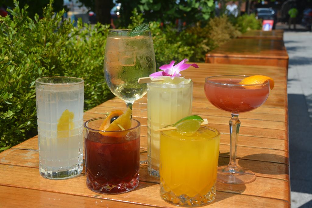 An assortment of colorful cocktails on a wooden table, surrounded by lush greenery.