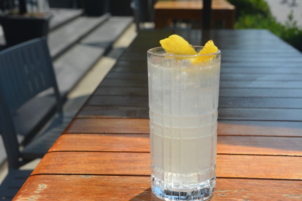 A glass of clear liquid garnished with lemon slices, sitting on a wooden table outdoors.