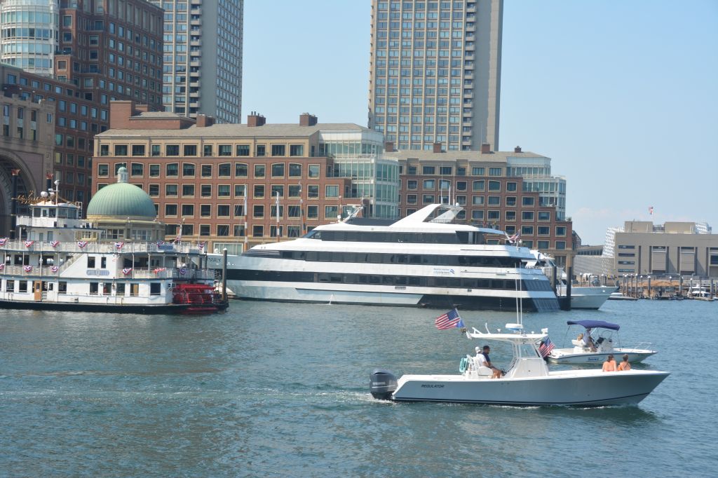 A large white yacht docked in a harbor, with smaller boats and buildings in the background.