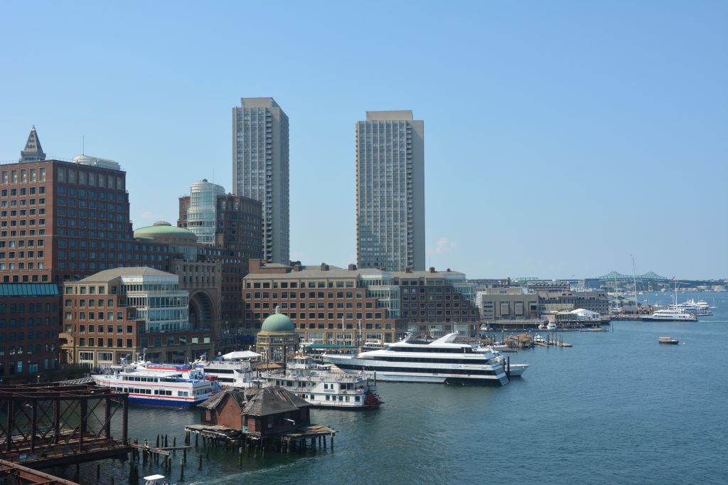 Cityscape with high-rise buildings, boats, and a cruise ship in the harbor of a coastal city.