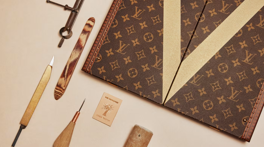 A Louis Vuitton monogram pattern book with various leather tools and accessories arranged on a beige background.