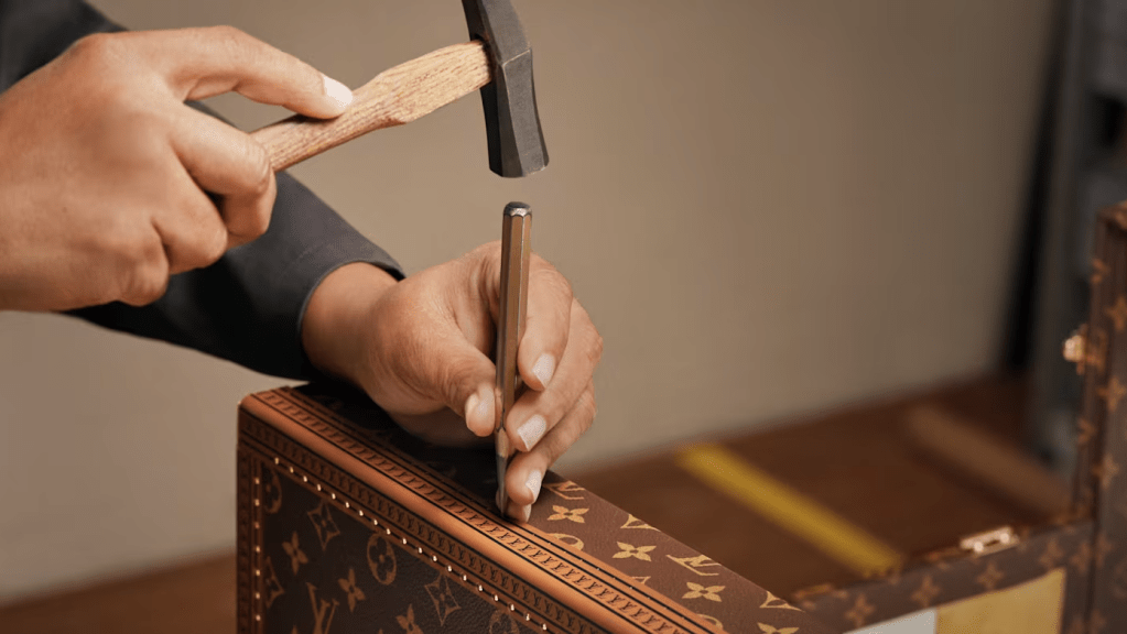 Hands using a hammer and nail to assemble a wooden box with decorative patterns.