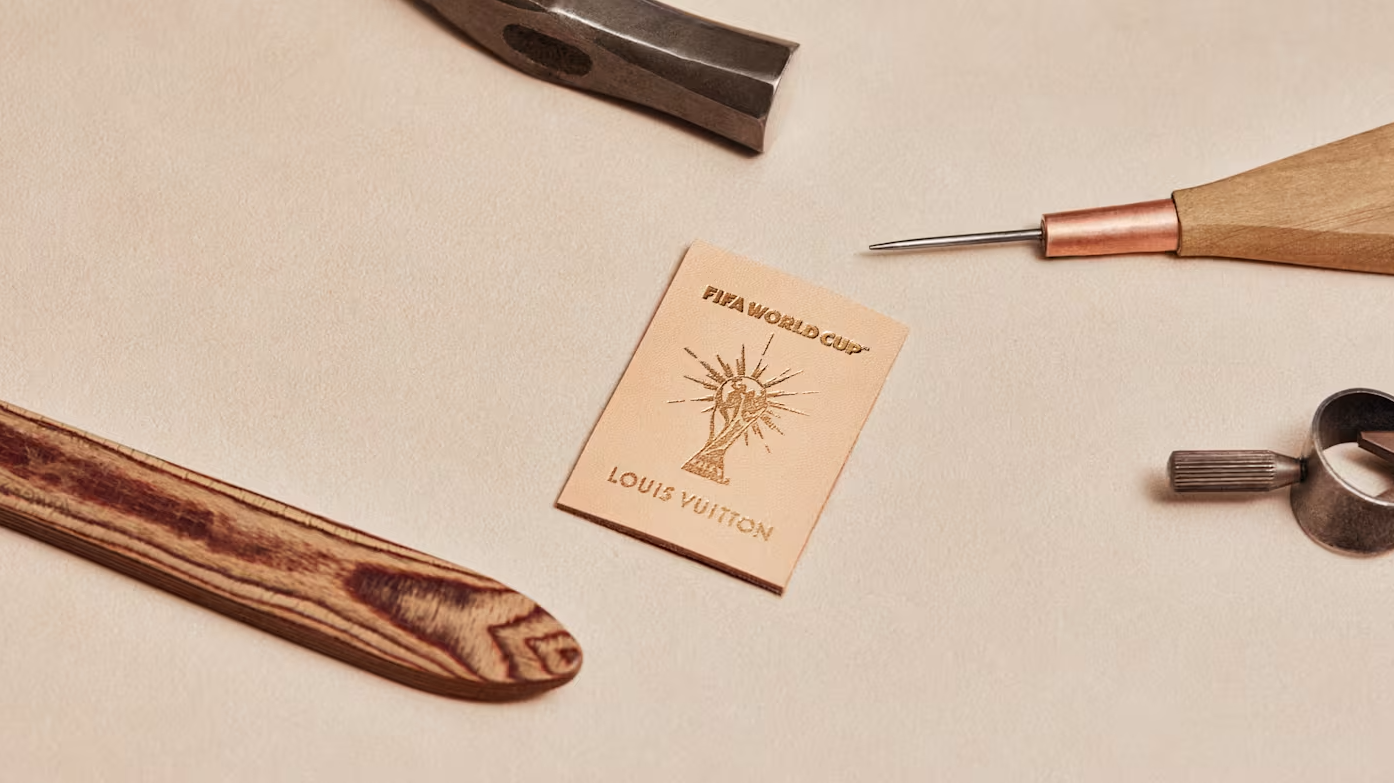 A wooden tool, a Louis Vuitton logo, and other workshop items on a beige surface.